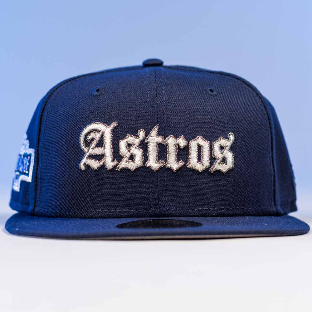 The Fat Elvis OE ASG Dark Blue New Era Hat 5950 Fitted features “Astros” embroidered in white gothic letters on the front, shown from the front against a light blue background.