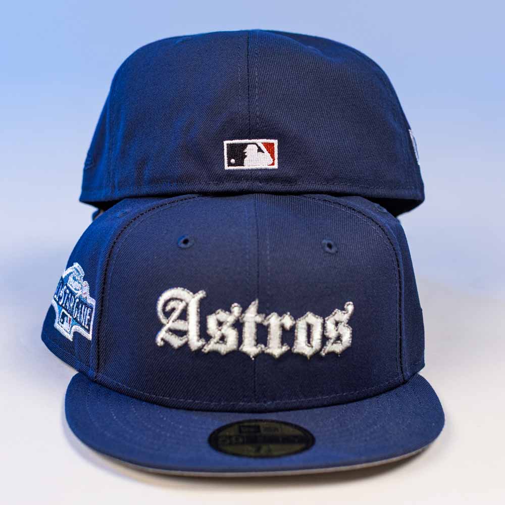 Two Fat Elvis OE ASG Dark Blue New Era Hat 5950 Fitted caps are stacked. The front cap features "Astros" embroidered in white with a side patch, while the back cap displays the MLB logo. Both have flat brims for a classic look.