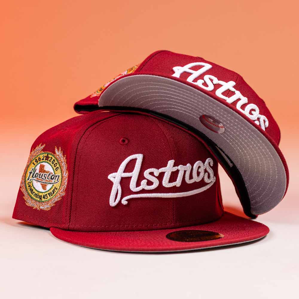 Two Big Puma Cardinal White Script New Era Hat 5950 Fitted caps are shown, one flat and one stacked. They feature embroidered Astros text and a 45th anniversary patch, set against a gradient orange background.