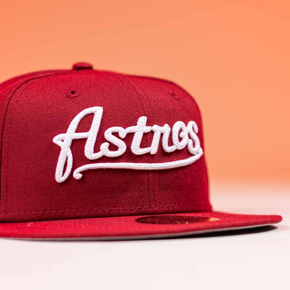The Big Puma Cardinal White Script New Era Hat 5950 Fitted features a vibrant red design with "Astros" in cardinal white script on the front, inspired by Big Puma and set against a light orange background.