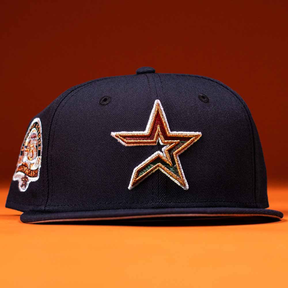 The Highclass 45th Houston Astros New Era Hat 5950 Fitted is a navy blue fitted cap featuring an embroidered gold, orange, and white Astros star logo on the front and a colorful side patch, shown against an orange background.