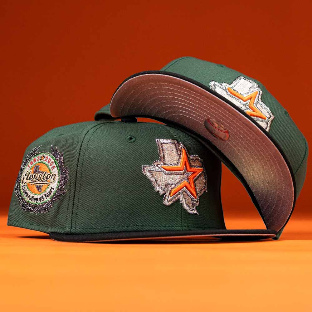 Two green El Jager Mountain Orange New Era 5950 Fitted hats with Texas-themed patches: one has a Houston badge on the side, the other shows a Texas outline with an orange star and Astros logo. Orange background.