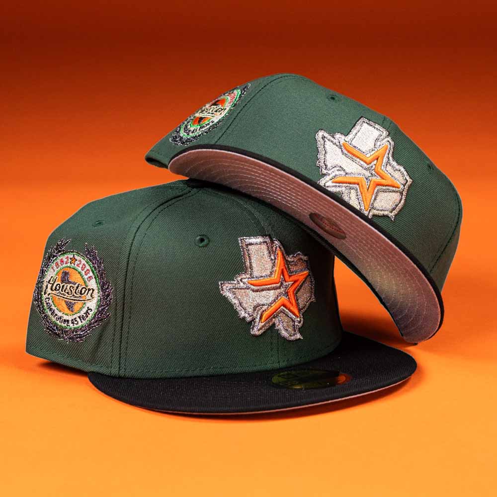 Two El Jager Mountain Orange New Era 5950 Fitted Hats, featuring green fabric, Texas-shaped patches with an orange star, and a "Houston" badge on the side, are set against an orange background—one lies flat while the other is propped on top.