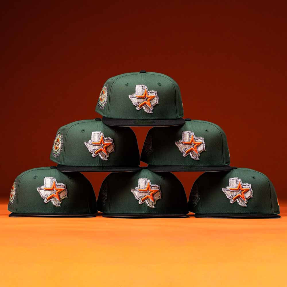 Six El Jager Mountain Orange New Era Hat 5950 Fitted caps are stacked in a pyramid against an orange background, each featuring a Texas state outline and star patch on the front.