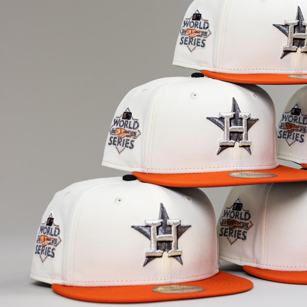 A stack of Orange Soda New Era WS22 Houston Astros 5950 Fitted hats, each with orange brims, the Astros star logo on the front, and a World Series patch on the side, displayed against a plain background.