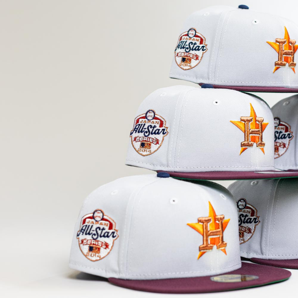 Four Shibuya Lights New Era Silver Japan Houston Astros 5950 Fitted hats are stacked, each with a purple brim, orange Astros logo, and an MLB All-Star Series patch. The background is plain and light-colored.