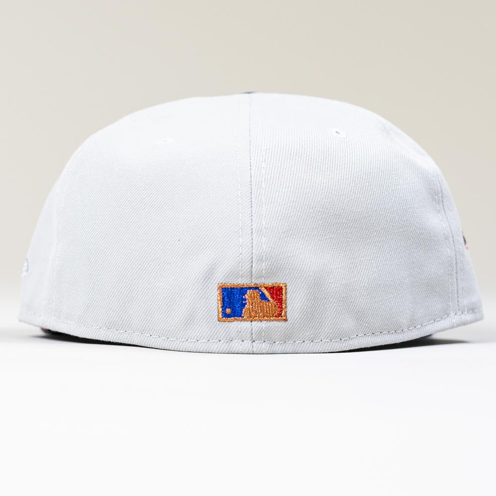 A close-up of the back of a white Shibuya Lights New Era Silver Japan Houston Astros 5950 Fitted cap showcases a small, embroidered MLB logo in blue, white, and red above the brim against a plain light background.