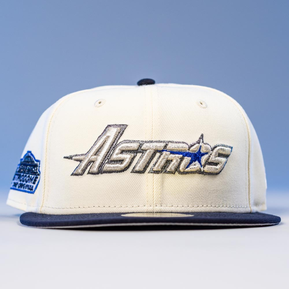The International Flea Bo Bundy New Era Houston Astros 5950 Fitted Hat features a white and navy design, Astros metallic embroidery on the front, a commemorative patch on the left, and a light blue-to-white gradient background.