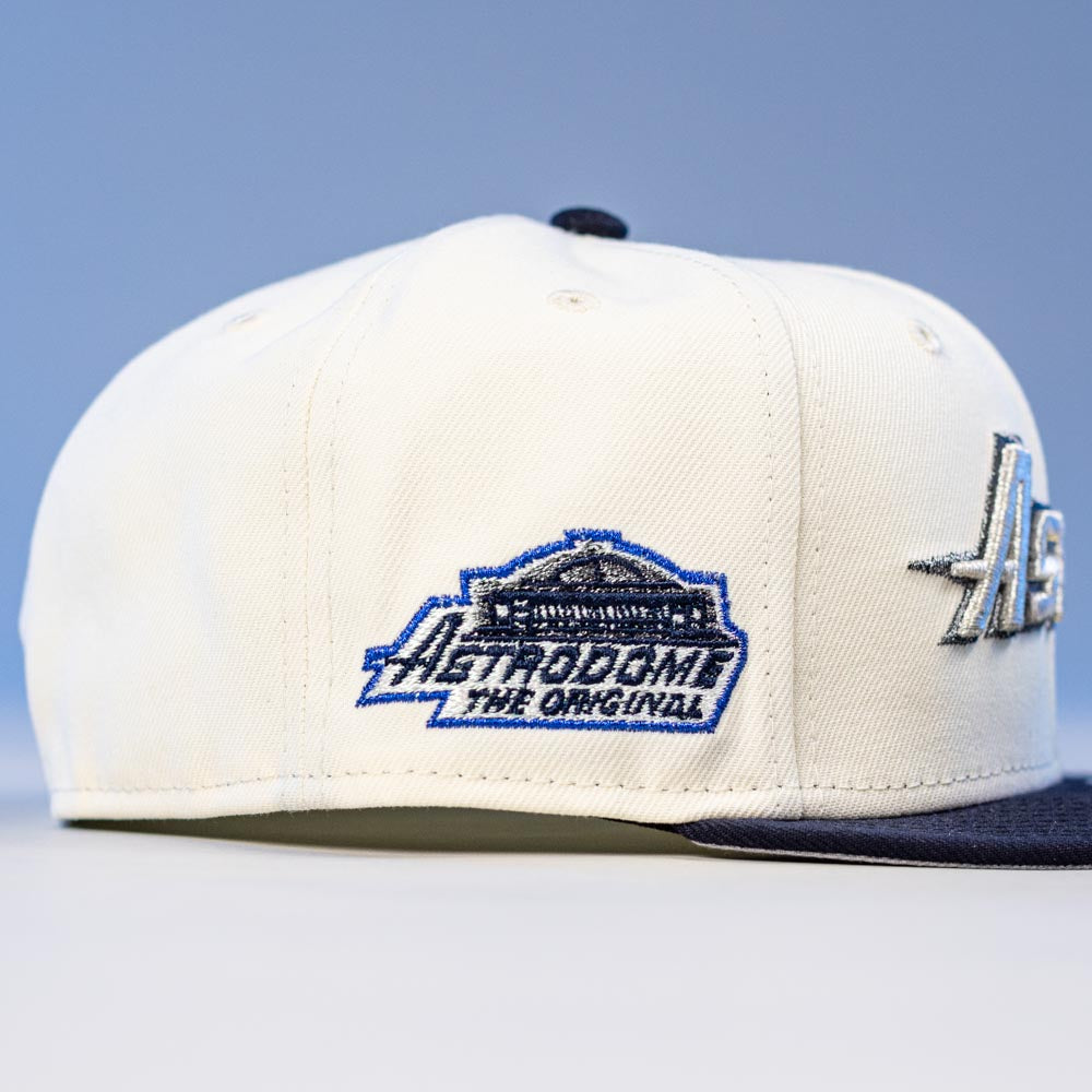 The International Flea Bo Bundy New Era Houston Astros 5950 Fitted Hat is white with blue trim, features an embroidered building and "Astrodome The Original" text on the side, set against a soft, blurred blue background celebrating Astros heritage.