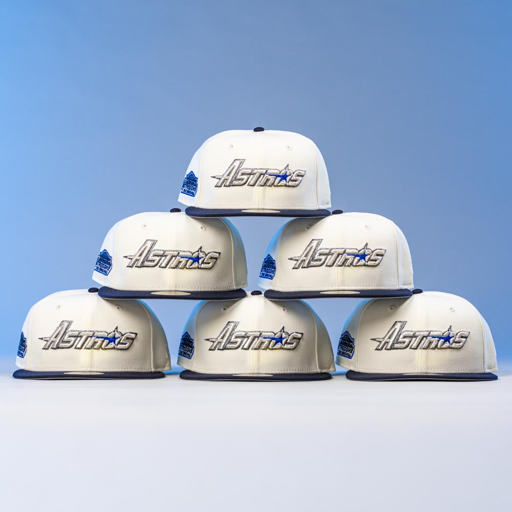 Six white and navy International Flea Bo Bundy New Era Houston Astros 5950 Fitted caps are stacked in a pyramid on a light blue background, each displaying the signature Astros logo on the front.