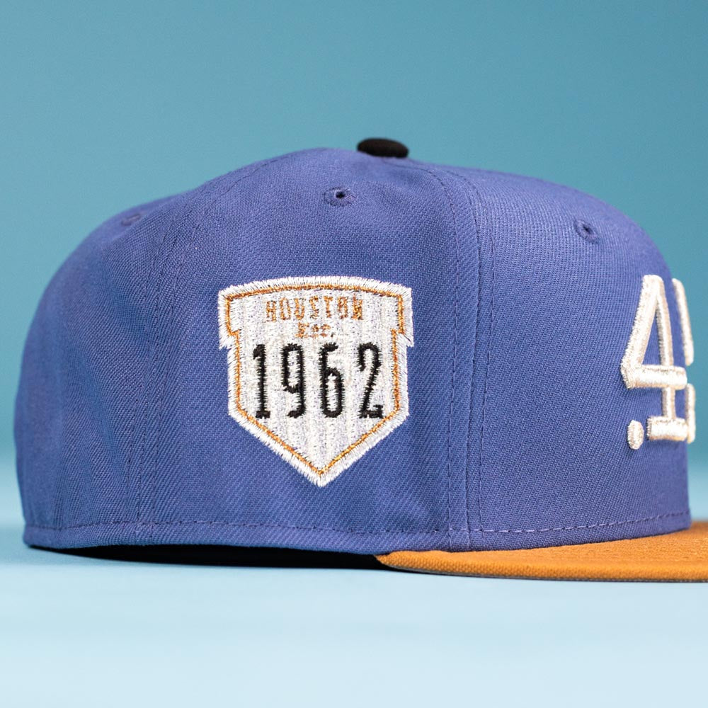 The Harbor Mark Canvas Houston Astros New Era Hat 5950 Fitted is blue with a yellow brim and a white side patch that says HOUSTON 1962 in black and gold. The hat sits against a solid light blue background.