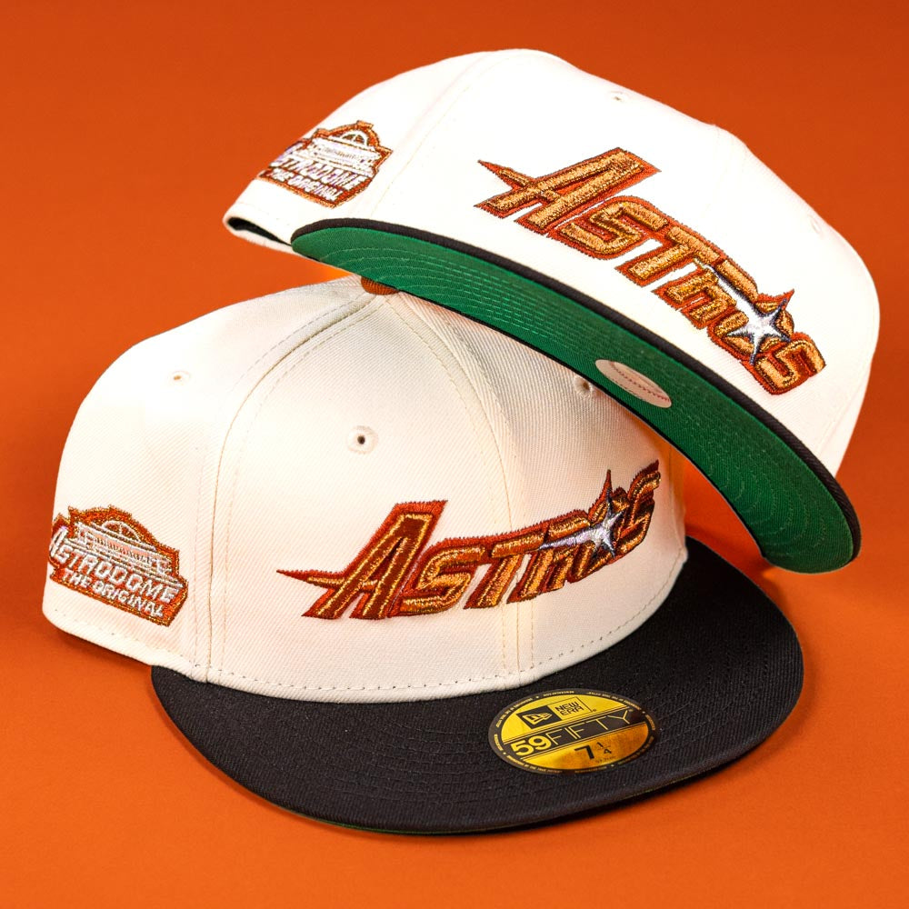 Two Rustic Sunset Houston Astros 5950 Fitted New Era hats are displayed on an orange background—both feature gold and orange logos; one has a black brim, while the other shows a green underside and rests tilted atop the first.