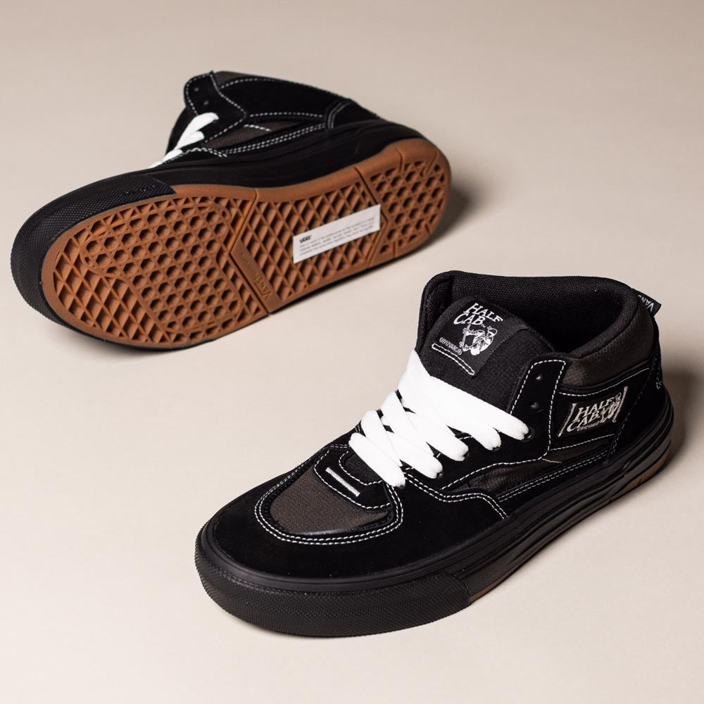 The VN000D9ZKOU Black Asphalt Suede Skate Wafflecup Half Cab Vans Shoes feature a black mid-top design with white stitching, white laces, brown Wafflecup-patterned soles, and visible brand logos on the tongue and side.