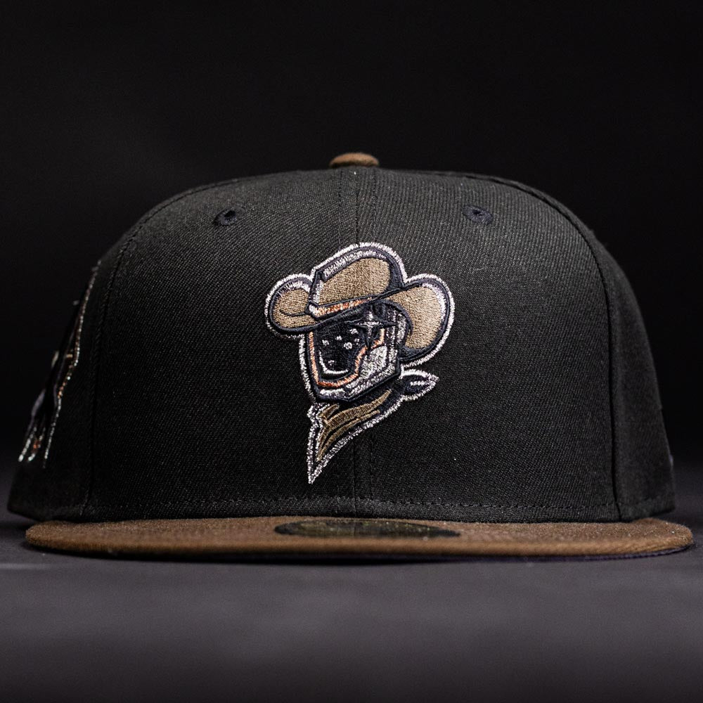 The Midnight Cowboy Sugarland Space Cowboys New Era 5950 Fitted Hat features a black walnut cap with a brown brim and an embroidered Space Cowboys logo—a cowboy in a hat and bandana—on the front, set against a dark background.