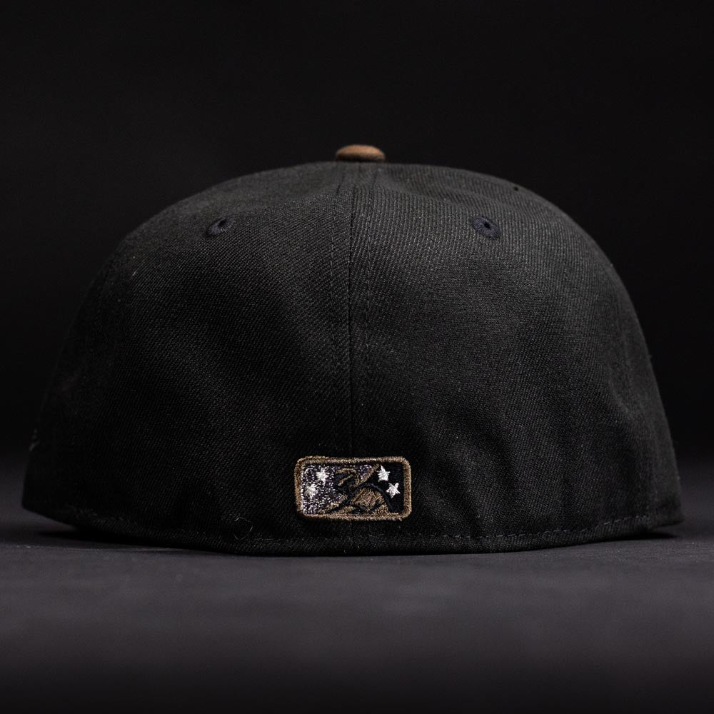 The Midnight Cowboy Sugarland Space Cowboys New Era 5950 Fitted Hat is shown from the back, featuring a small gold and black star and figure patch near the bottom—subtly referencing the Space Cowboys. The hat and background are both black.