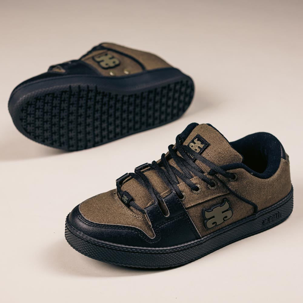 The Cricket Green Waxed Hemp I Path Skateboarding Shoes feature greenish-brown hemp canvas uppers, black accents, black rubber soles, and a stylized logo on the side and tongue. One shoe stands upright, with the other lying on its side.