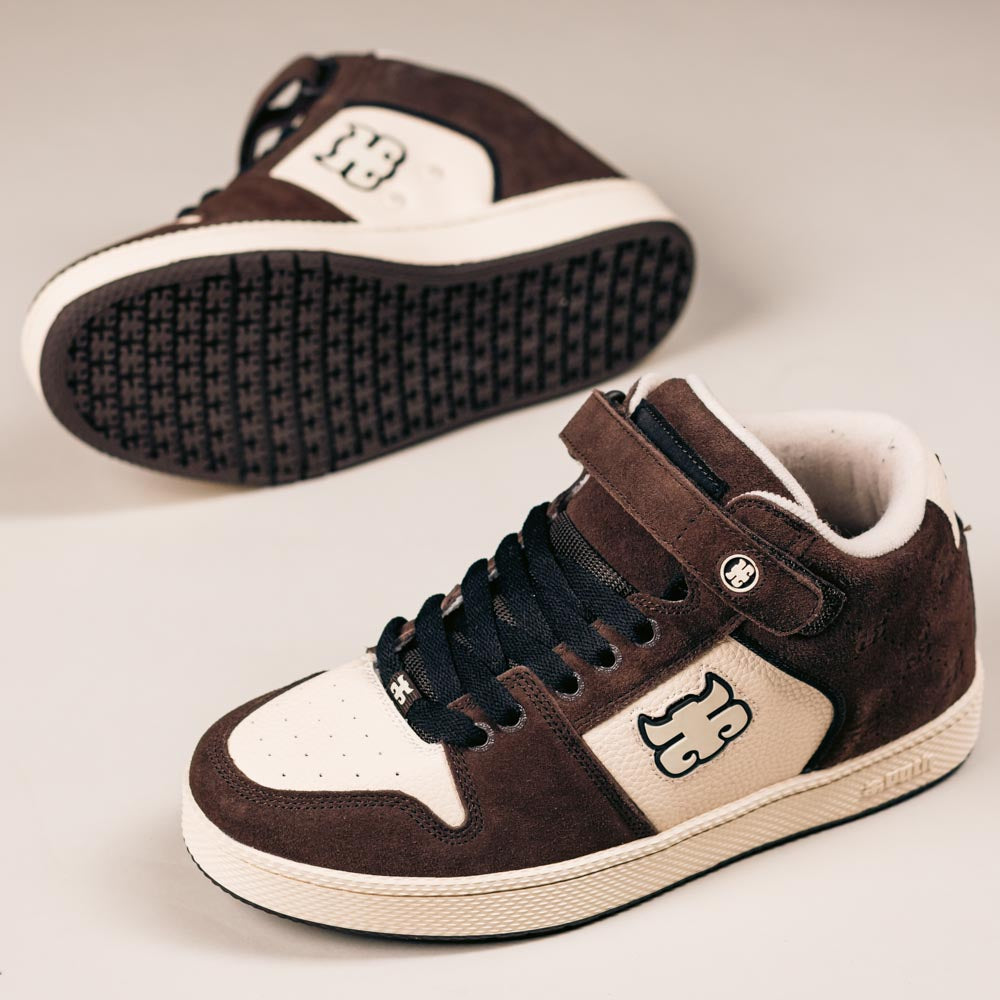 The Grasshopper Brown Suede Leather I Path Shoes Skateboarding feature a mid-top design, black laces, a Velcro strap, and a distinctive logo on the side—one upright, one on its side to display the sole.