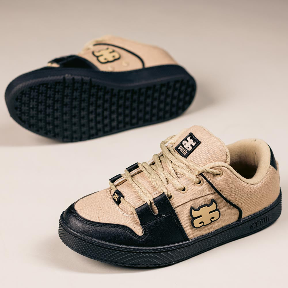 The Cricket Natural Hemp I Path Shoes Skateboarding are beige and black sneakers with a distinctive beige logo, hemp synthetic material, and cupsole construction. One shoe stands upright, the other lies behind it, both on a light surface.