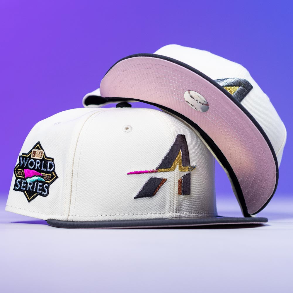 Two white Trilltiberi Rushmore WS22 Chrome Graphite Houston Astros New Era 5950 Fitted hats are shown, each with black brims. One displays a stylized A logo, the other a World Series patch. Pink underbrim with embroidered baseball. Purple background.