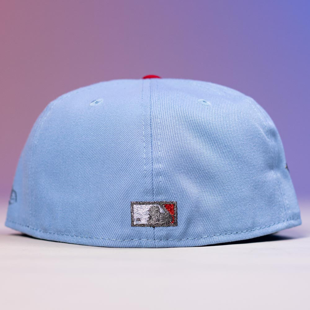The Sicko Mode Rushmore 2017 B Blue Black Houston Astros New Era Hat 5950 Fitted is displayed from the back, showcasing a rectangular patch with a bear and red triangle. The softly lit background glows in purple and pink hues.