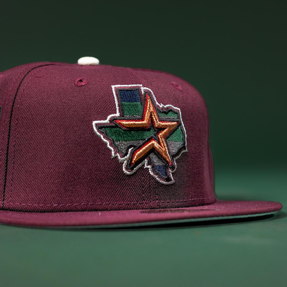 The Pinkerton 2.0 Rushmore 2000 Maroon Houston Astros New Era Hat 5950 Fitted features an embroidered Texas outline with a multicolored, stylized star on the front, inspired by Astros colors and set against a dark green background.