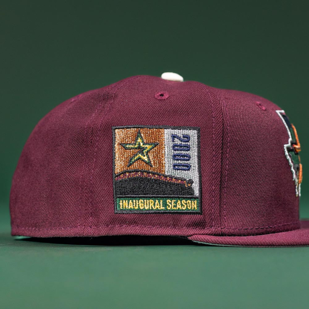 The Pinkerton 2.0 Rushmore 2000 Maroon Houston Astros New Era 5950 Fitted Hat features a side patch with a yellow and green star, the year 2000, and INAUGURAL SEASON, shown on a solid green background.