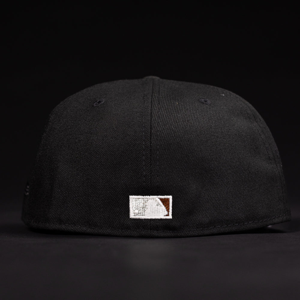 The La Flame Rushmore WS05 Fire Black Houston Astros New Era 5950 Fitted Hat is shown from the back, displaying a small rectangular patch with white and brown stitching near the bottom edge. The background is black.
