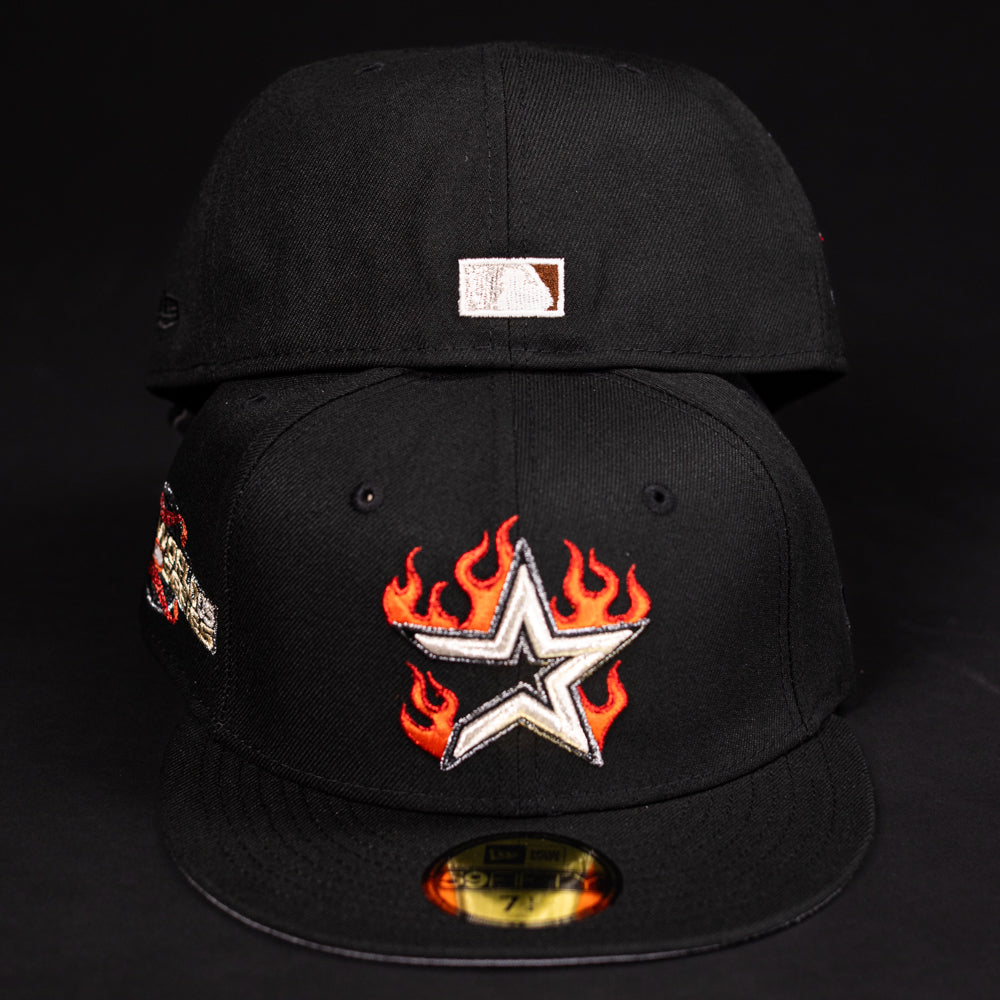 Two black La Flame Rushmore WS05 Fire Black Houston Astros New Era Hat 5950 Fitted caps on a black background—one displays a silver star with red-orange flames, and the other has a small white and brown logo on the back.
