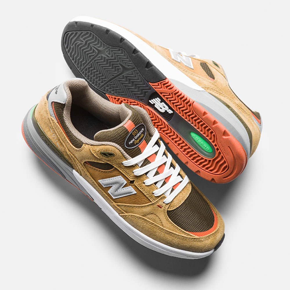 A pair of 933 MNO Andrew Reynolds Brown Grey New Balance Numeric Suede Skateboarding Shoes, featuring white laces, orange accents, and green sole details, is displayed on a light gray background with one shoe upright and one showing the sole.