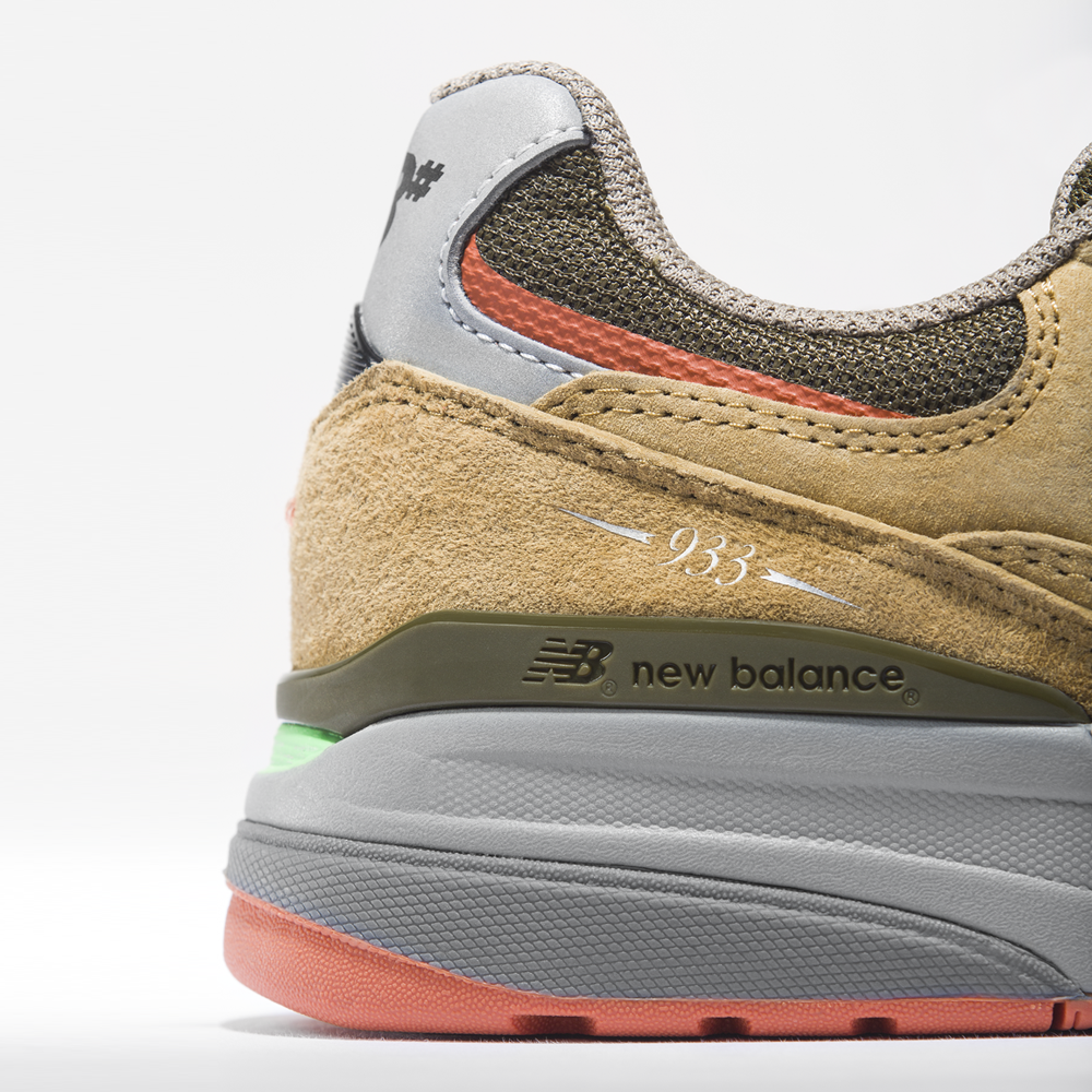 Close-up of the heel of the New Balance Numeric 933 MNO Andrew Reynolds skateboarding shoes in brown suede with grey accents, featuring white arrow detailing and a logo that highlight its skate-inspired design.