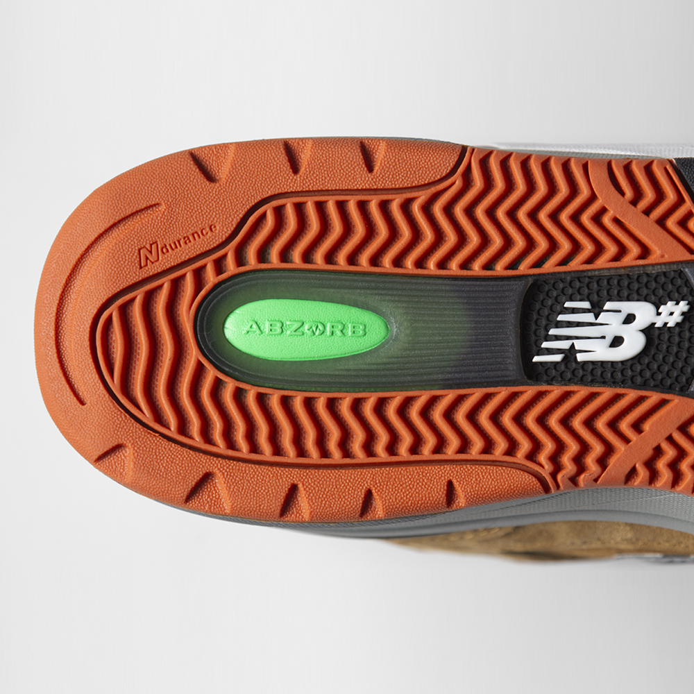 Close-up of the sole of the 933 MNO Andrew Reynolds Brown Grey New Balance Numeric Skateboarding Shoes Suede, showing an orange tread, green ABZORB insert, and white New Balance branding on a black heel section.