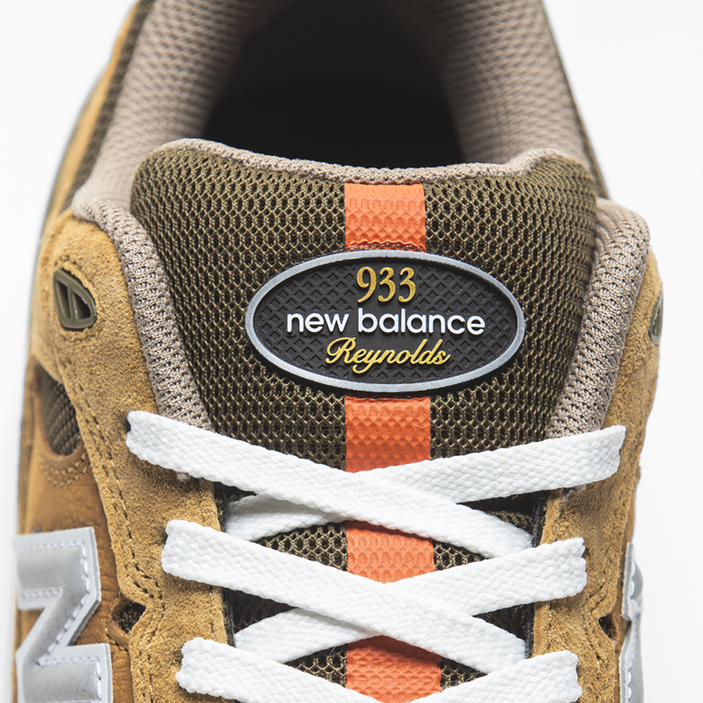 Close-up of 933 MNO Andrew Reynolds Brown Grey New Balance Numeric Skateboarding Shoes with tan suede, white laces, olive green mesh, orange stripe, and tongue label reading "933 new balance Reynolds" in white/yellow.