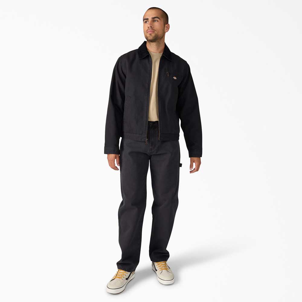 A man with short hair and a trimmed beard stands against a white background, wearing the A8702 Black Blanket Lined Painter Canvas Jacket Dickies Skateboarding with matching pants, a beige t-shirt, and beige sneakers, looking slightly to the side.