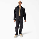 A man with short hair and a trimmed beard stands against a white background, wearing the A8702 Black Blanket Lined Painter Canvas Jacket Dickies Skateboarding with matching pants, a beige t-shirt, and beige sneakers, looking slightly to the side.
