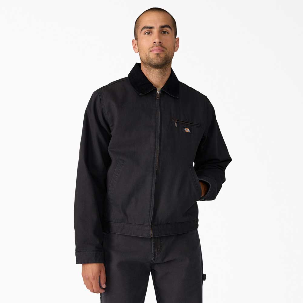 A man wears the A8702 Black Blanket Lined Painter Canvas Jacket by Dickies Skateboarding with matching black pants, standing against a white background and looking straight ahead with a neutral expression.