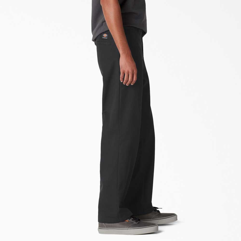 A person stands sideways against a plain white background, showcasing only the lower half of their body while wearing Dickies Skateboarding A8768 Regular Fit Twill Pant in black and gray sneakers.