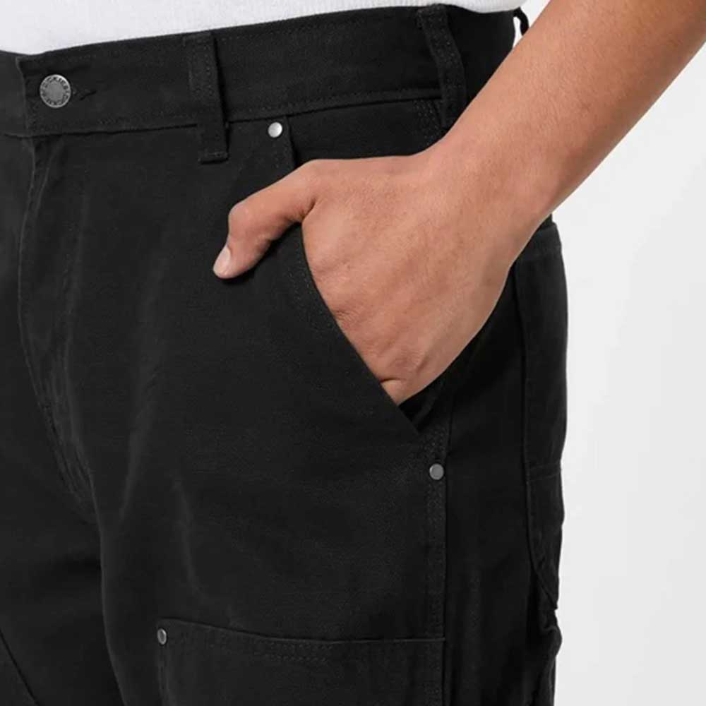 A person wearing A87PE Black Double Knee Canvas Carpenter Pant Dickies Skateboarding, standing with one hand in the front pocket, shown from the waist down against a plain background.