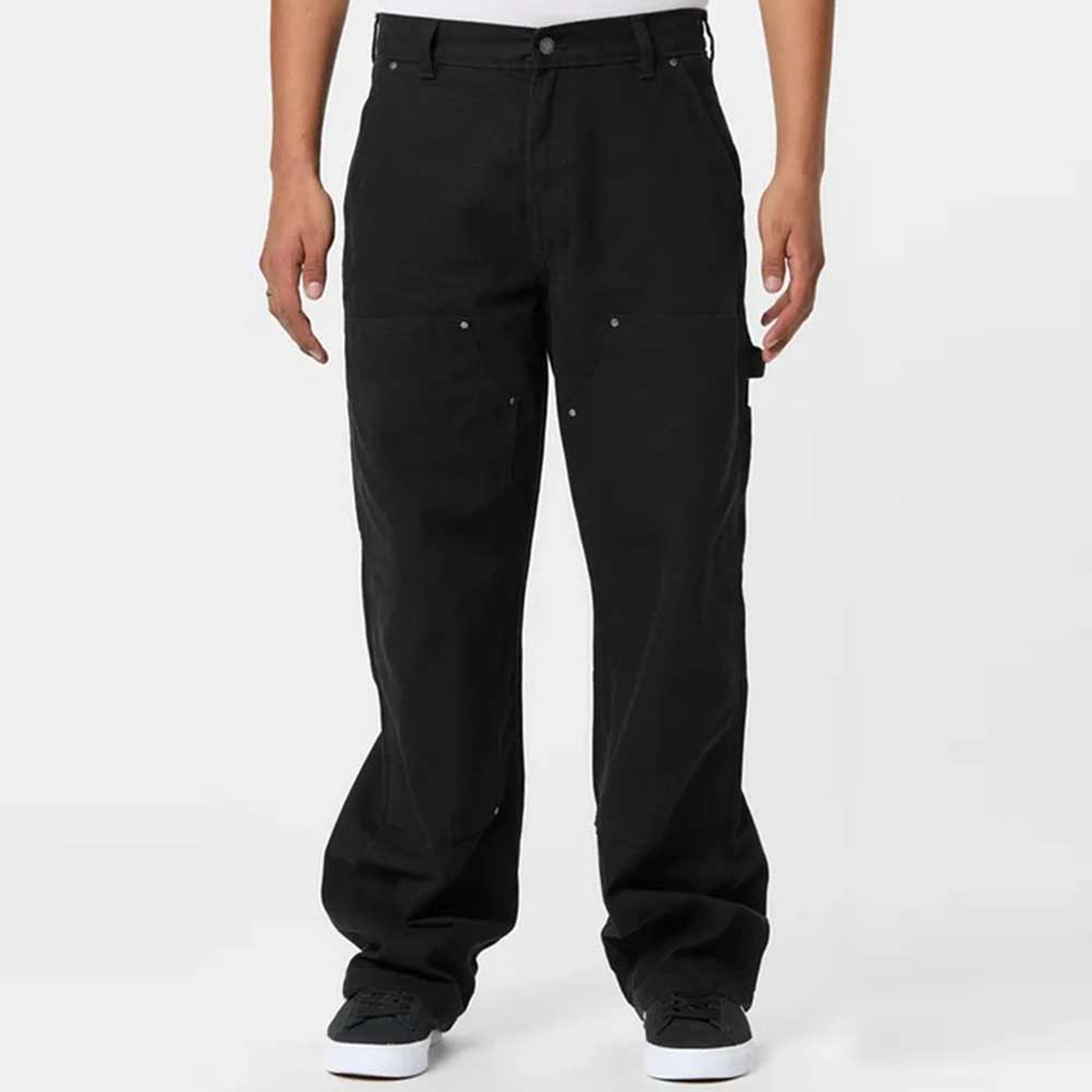 A person stands facing forward, wearing A87PE Black Double Knee Canvas Carpenter Pant Dickies Skateboarding and black-and-white sneakers, hands relaxed at their sides against a plain white background.