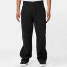 A person stands facing forward, wearing A87PE Black Double Knee Canvas Carpenter Pant Dickies Skateboarding and black-and-white sneakers, hands relaxed at their sides against a plain white background.
