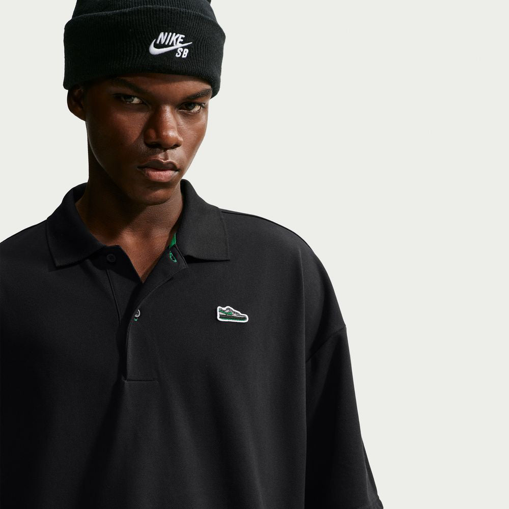 A person wearing a black Nike SB AF1 Black Court Green Solid Break Polo IV0597010 with a small sneaker emblem on the chest and a black beanie.