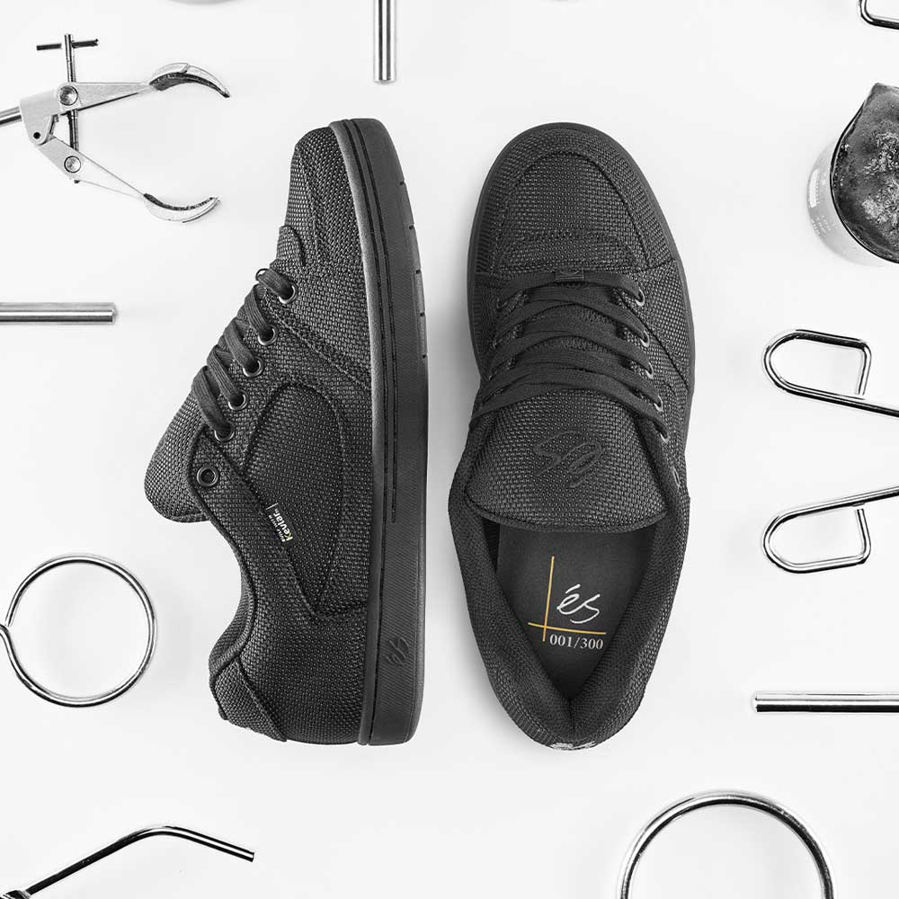 A pair of Accel Kevlar Black Es Skateboarding Shoes is displayed on a white background with metallic tools around. One shoe stands upright, the other lies on its side, showing an insole marked “001/300.”.