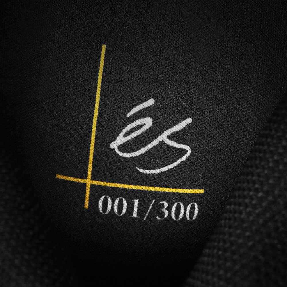 A close-up of the fabric label on Accel Kevlar Black Es Shoes Skateboarding shows a yellow line over a white one, handwritten "és," and "001/300" below, set against black fabric reflecting its skateboarding roots.