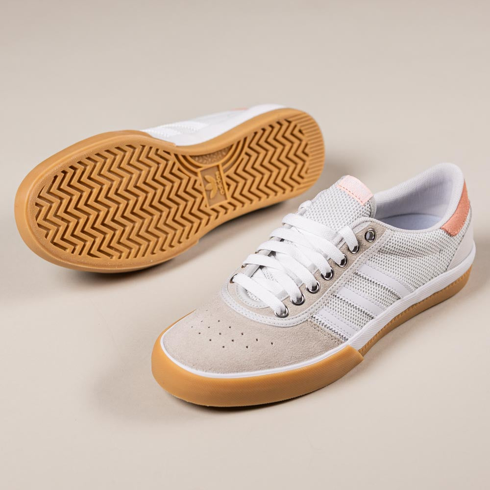 The Lucas Premiere White Coral HQ7524 Adidas Skateboarding suede shoes feature white mesh and suede uppers, three white side stripes, gum rubber soles, and a light peach heel accent. One shoe displays the sole, inspired by Lucas Premiere design.