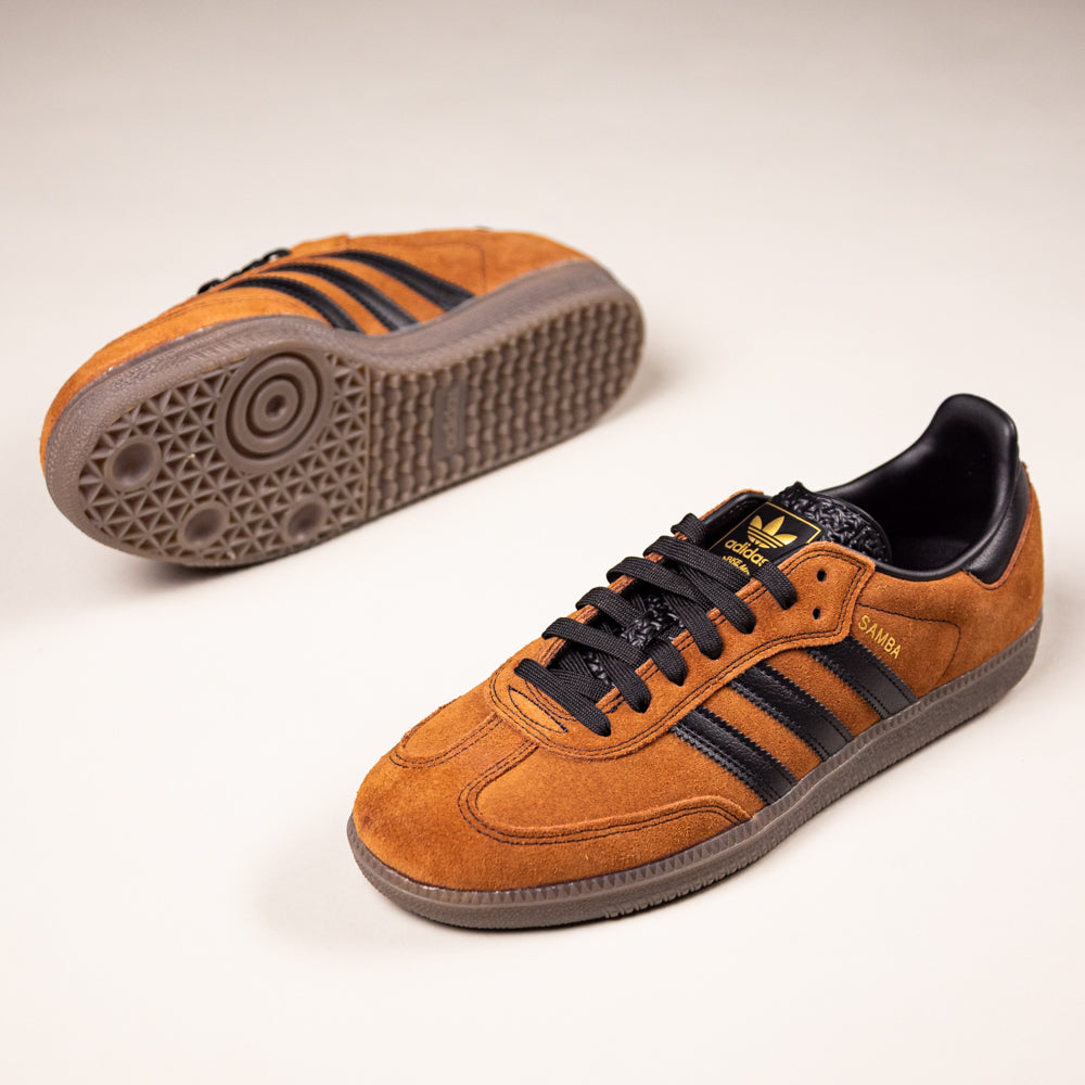 The Samba ADV Brown Black HQ9286 Adidas Skateboarding Shoes feature a suede and premium leather upper, black stripes, and a textured sole; one shoe lies flat while the other is upright.