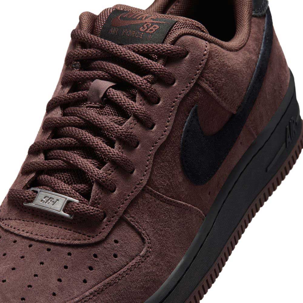 Close-up of the Air Force 1 Black Light Chocolate HM8517201 Nike SB Suede Skateboarding Shoe featuring a brown suede upper with a black Nike Swoosh, textured finish, perforated toe box, and matching black sole. Designed as a premium skate shoe, this model includes laces with a metal SB-engraved tag and delivers outstanding comfort through its signature Nike Air cushioning.