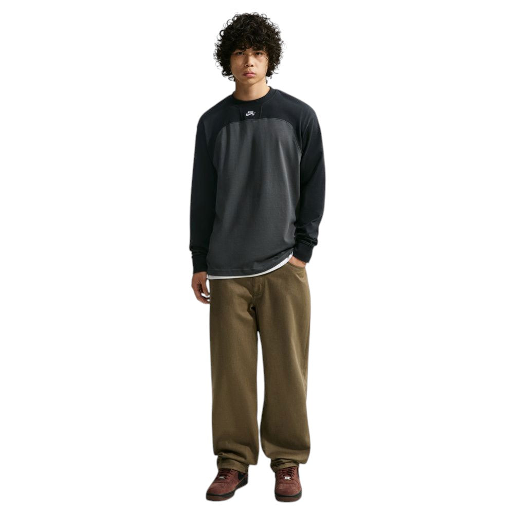 A man wearing a black and gray color-blocked Airmail Longsleeve IM5430060 Black Gray Skate Longsleeve T-Shirt SB Tee Skate Nike SB Skateboarding and olive-green pants.