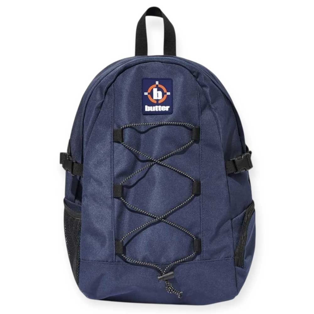 The Aleka Backpack Navy by Butter Goods features navy blue nylon canvas, black zippers, adjustable straps, a front bungee cord, side mesh pockets, and a top patch with the Butter logo.
