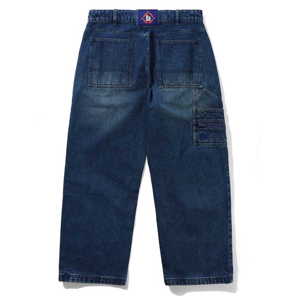 The Aleka Dark Indigo Denim Jeans by Butter Goods are loose fit cotton jeans with large carpenter pockets, a right-side utility loop, and a purple belt featuring a circular red and blue buckle, shown laid flat on a white background.