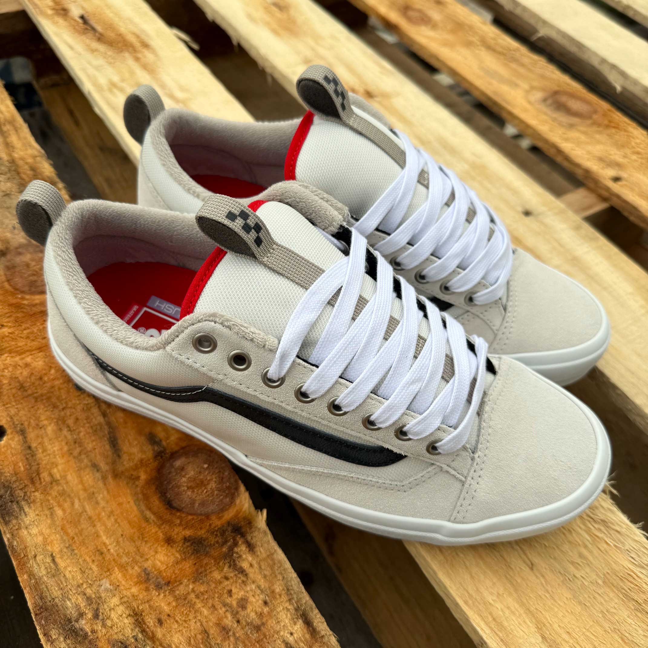 A pair of Antique White Black Skate Old Skool 36+ Vans Suede Shoes with white laces, red inner lining, and a black side stripe, displayed on a wooden pallet background.