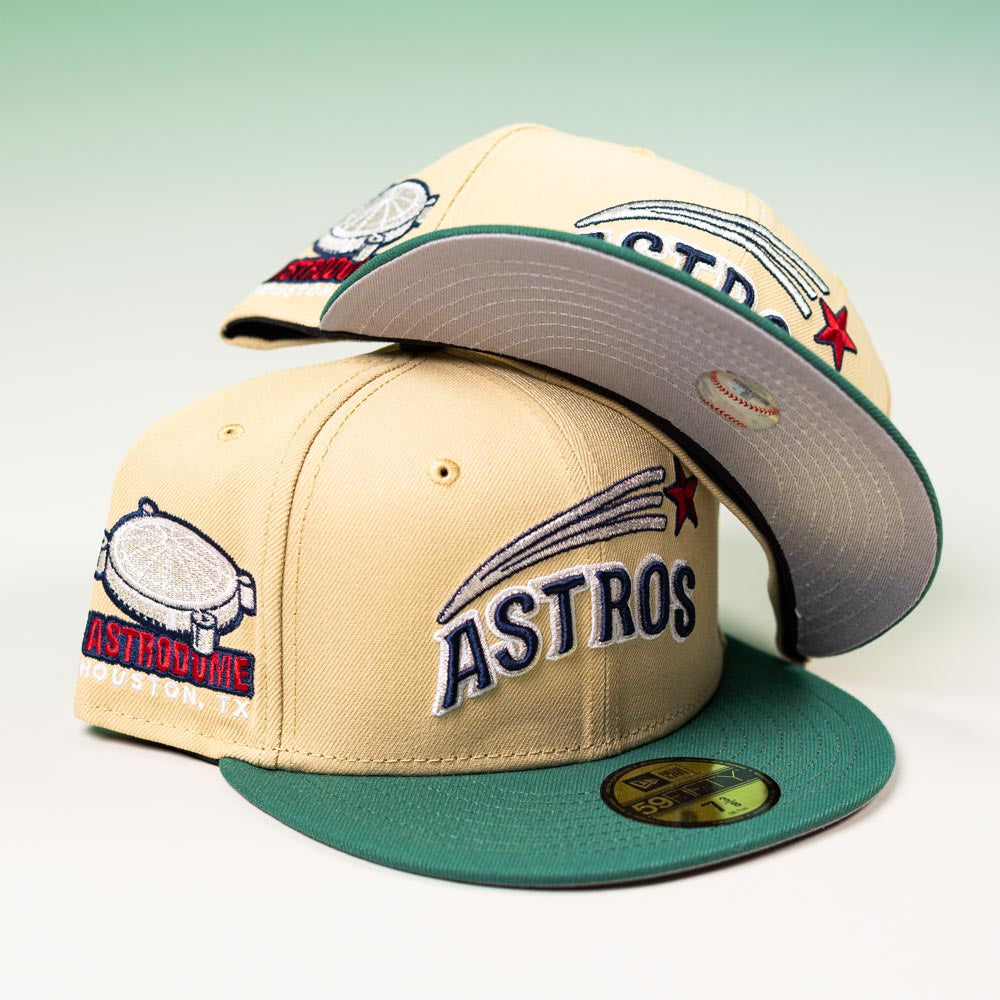 Two New Era 5950 Houston Astros Vegas Gold Emerald Aeros Day hats, featuring green brims and bold logos with Astrodome sidepatches, are stacked on a light surface against a gradient green background.